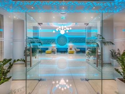 Heller Hotel-Lobby-Eingang mit Glasschiebetüren, moderner Beleuchtung und Pflanzen