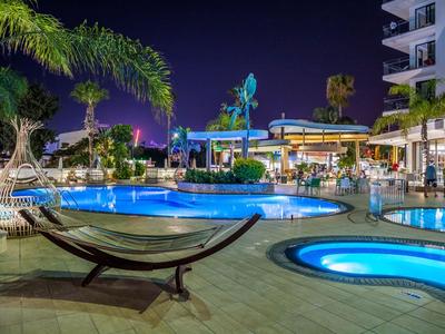 Hotelpool mit beleuchteten Whirlpools und einer Hängematte bei Nacht.
