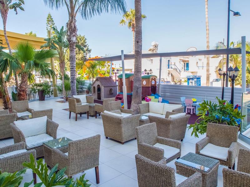 Outdoor hotel bar area with rattan chairs, tables, and palm trees in daylight.