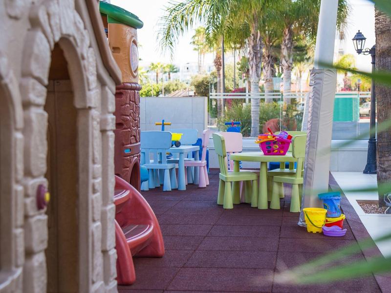 Colorful children's playground with tables, chairs, and sand toys under palm trees.