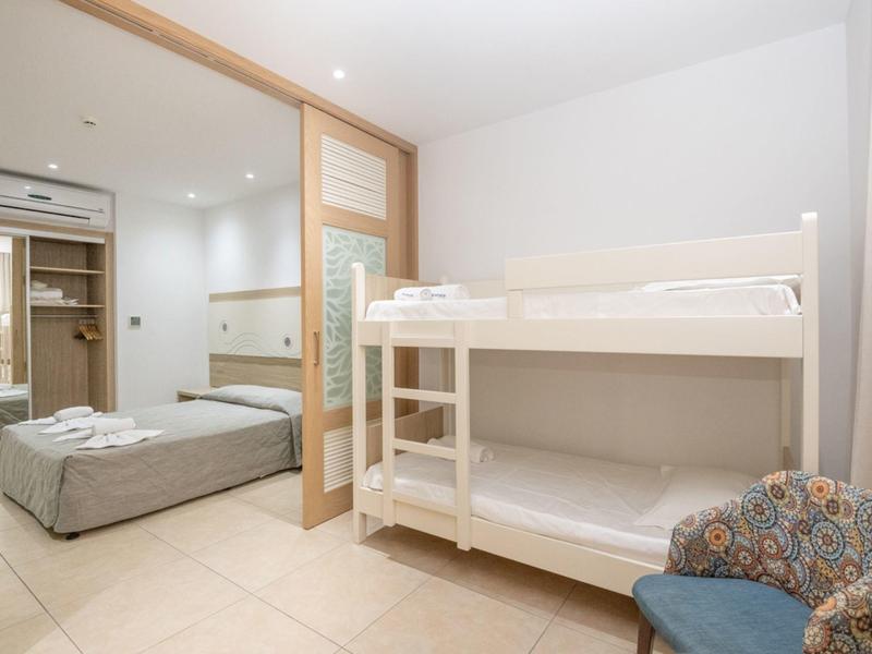 Hotel room with bunk bed, double bed, and cozy armchair in bright space.