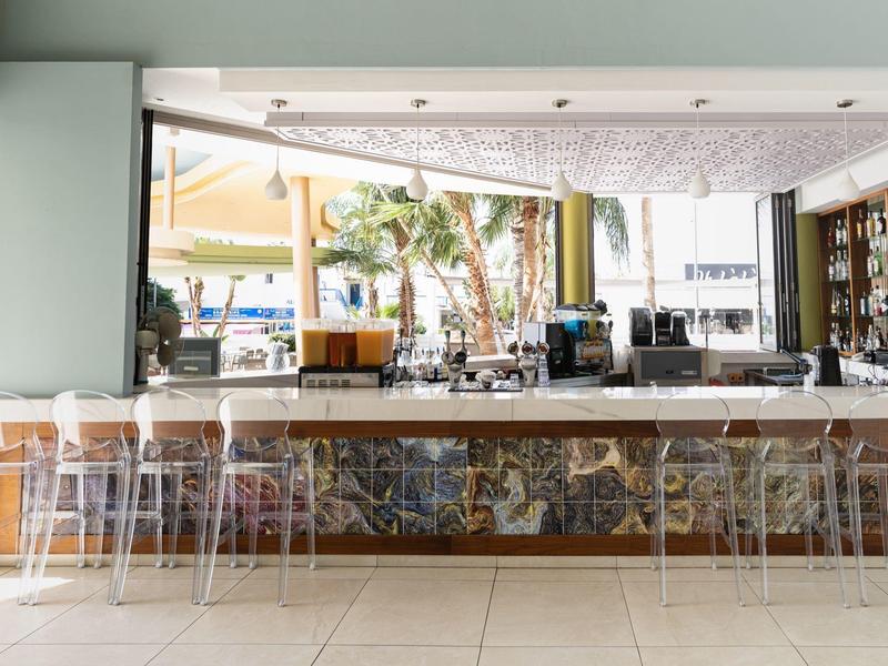 Empty modern hotel bar area with stools and open view to outdoor seating.