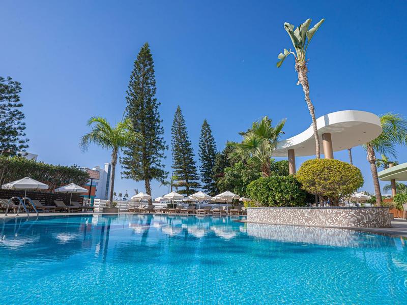 Large pool with sun umbrellas and tropical trees under clear blue sky.