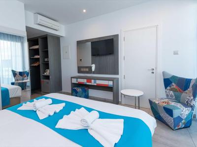 Helles Schlafzimmer mit blauen Akzenten, modernem Sessel, TV und kleinem weißen Beistelltisch.