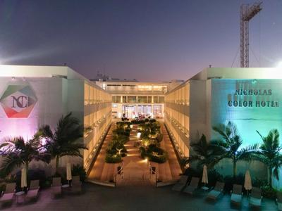 Modernes Hotel mit beleuchtetem Poolbereich und Palmen bei Dämmerung.