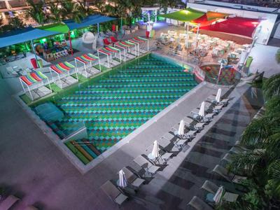 Beleuchteter Hotelpool mit Liegestühlen und bunten Sonnenschirmen am Abend.