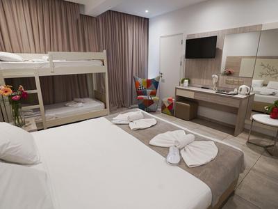 Nowoczesny pokój hotelowy z łóżkiem podwójnym, łóżkiem piętrowym, biurkiem, telewizorem, neutralną kolorystyką i prostym wystrojem.
