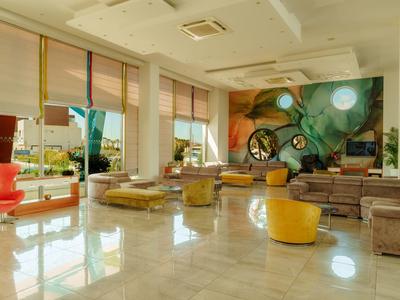 Jasny, nowoczesny pokój hotelowy z dużymi oknami, kolorową ścianą i wygodnymi siedzeniami.