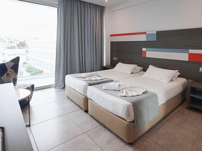 Nowoczesny pokój hotelowy z dwoma łóżkami, dużym oknem i szarymi zasłonami.