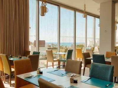 Nowoczesna restauracja hotelowa z kolorowymi krzesłami i dużymi oknami z widokiem na morze.