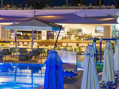 Moderner Außenbereich eines Hotels mit beleuchtetem Pool und Sitzgelegenheiten bei Nacht.