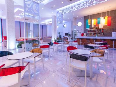 Modernes Café mit weißen Tischen, bunten Stühlen und heller, eleganter Beleuchtung.