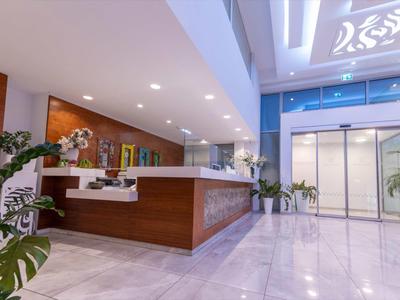 Moderne Empfangshalle mit Holztresen, weißen Wänden, großen Pflanzen und Glasaufzügen.