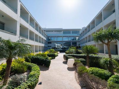 Moderner Hotelhof mit gepflegten Wegen, grünen Sträuchern und Palmen unter klarem Himmel.