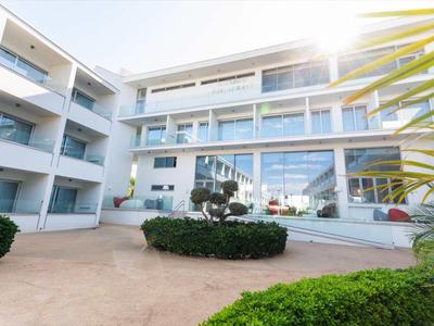 Modernes weißes Gebäude mit vielen Fenstern und begrüntem Innenhof bei Sonnenschein.