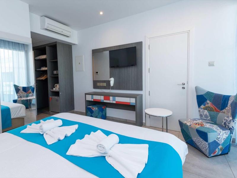 Helles Schlafzimmer mit blauen Akzenten, modernem Sessel, TV und kleinem weißen Beistelltisch.