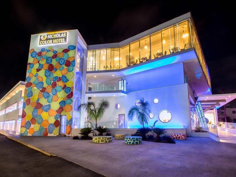 Modernes Gebäude mit bunter Fassade und großem, verglastem Obergeschoss bei Nacht.