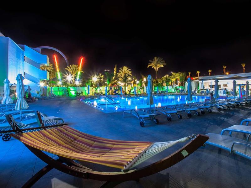 Nachtaufnahme eines beleuchteten Pools mit Liegen und Hängematte im Vordergrund.