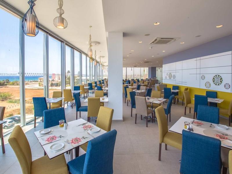 Moderner, heller Restaurantraum mit großen Fenstern, bunten Stühlen und sauber gedeckten Tischen.