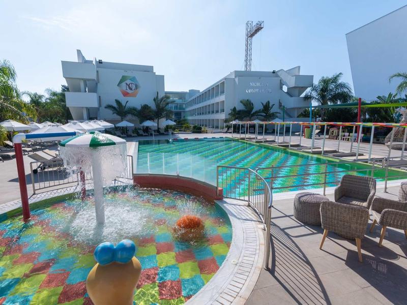 Ein Außenpoolbereich mit einem Kinderbecken vorne und einem größeren Pool dahinter, umgeben von Stühlen.