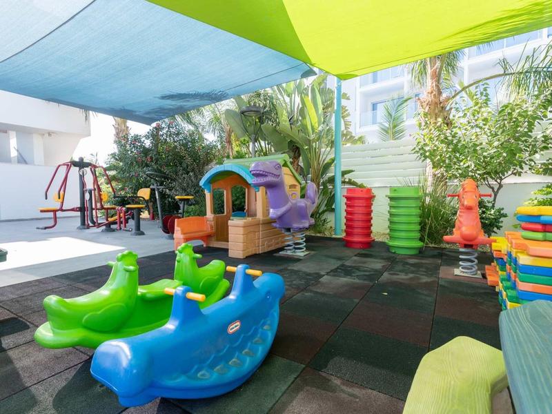 Bunter Kinderspielplatz mit Rutschen, Schaukeln und Sonnensegel im Außenbereich.