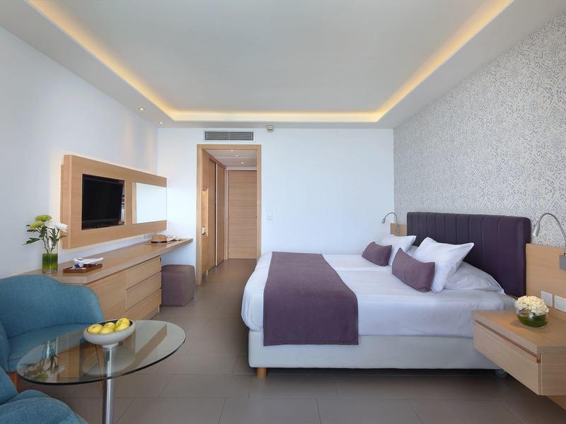 Modern hotel room with double bed, two armchairs, and a wall-mounted TV.