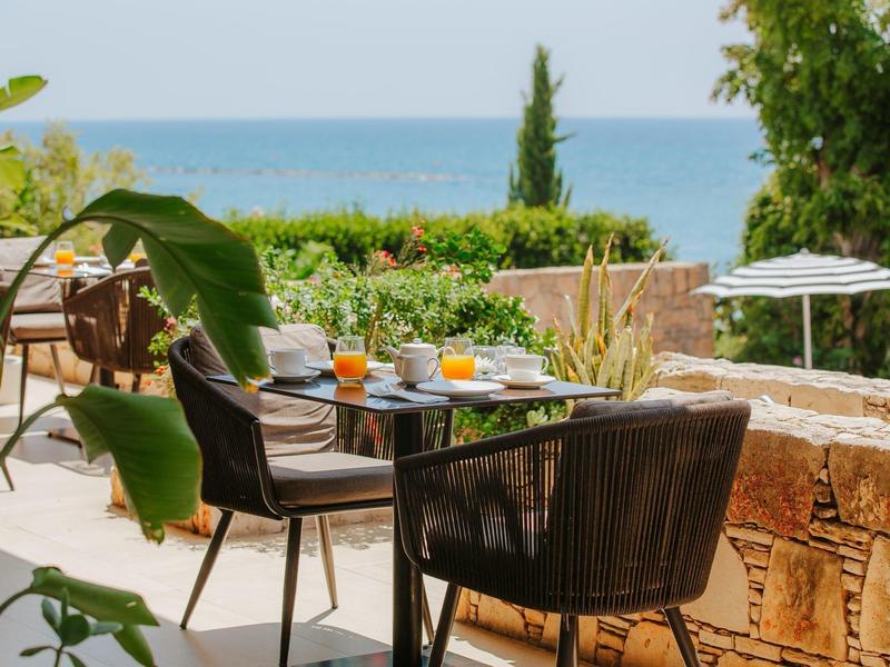 Terrace with table and chairs, breakfast setup overlooking the sea and greenery.