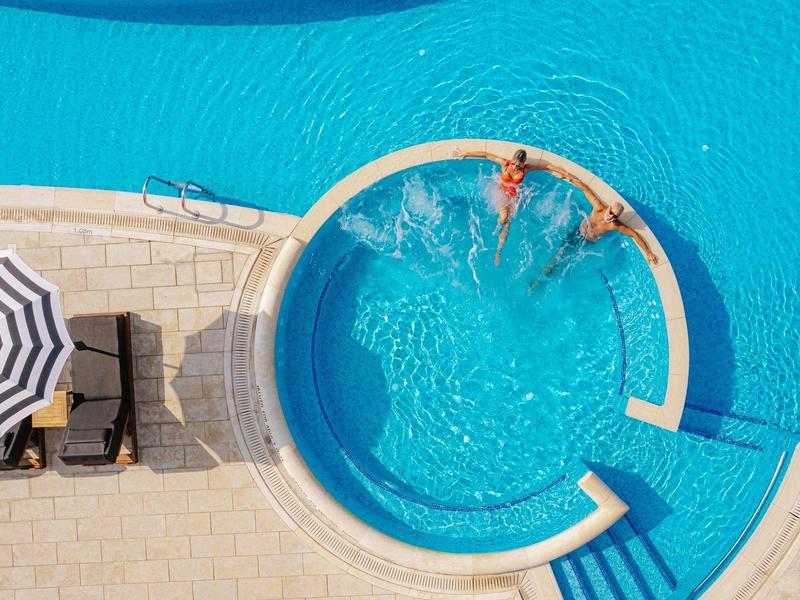 Three people enjoying a round pool with umbrellas and lounge chairs nearby.