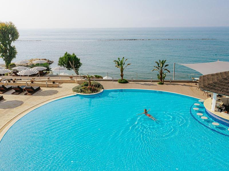 Large pool with person swimming, surrounded by loungers and a sea view.