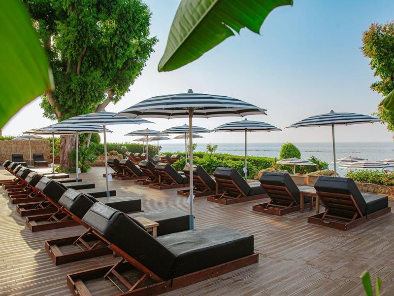 Sun loungers with umbrellas on wooden deck overlooking the sea and trees.