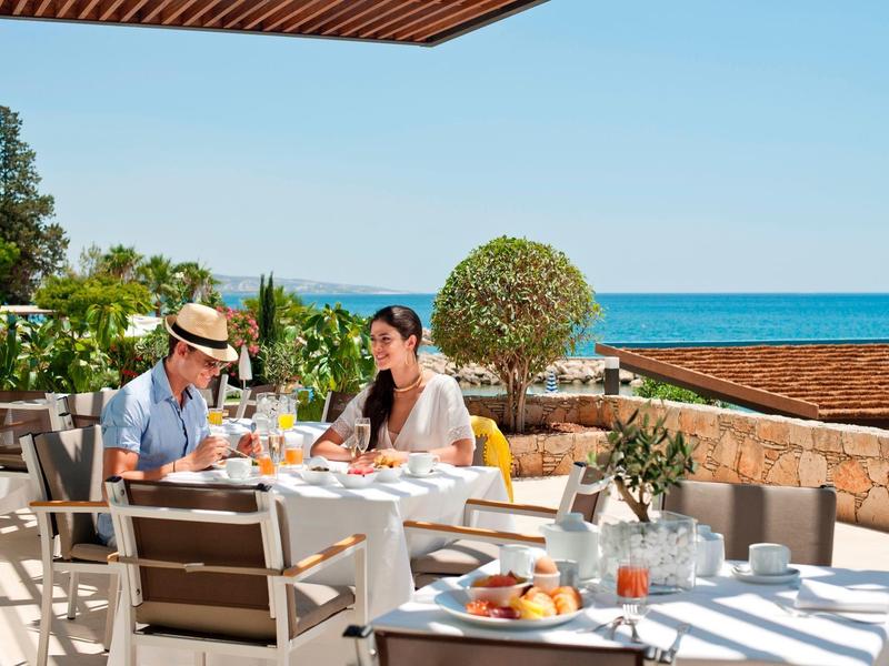 Couple enjoying breakfast on sunny terrace with sea view and Mediterranean surroundings.