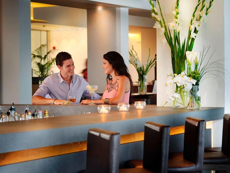 Couple sits comfortably at a hotel bar with warm ambiance and floral arrangement.