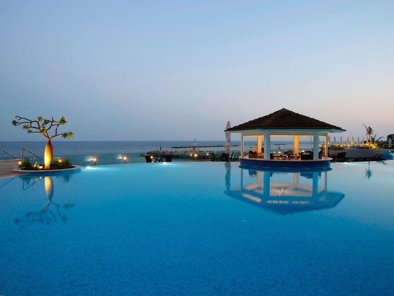 A calm pool with an illuminated pavilion and sea in the background at sunset.