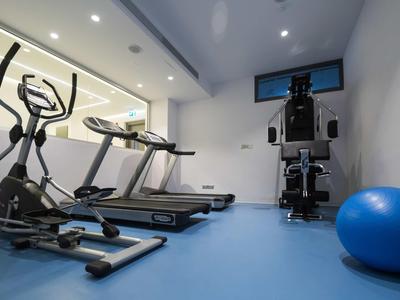 Palestra moderna con tapis roulant, ellittica e palla da ginnastica su pavimento blu.