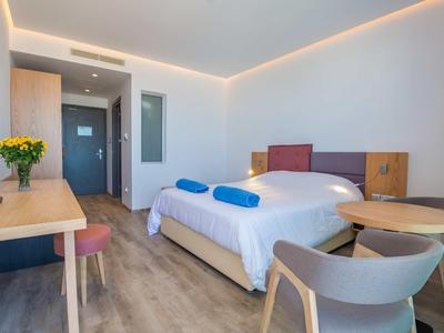 Helles Hotelzimmer mit Doppelbett, Holzmöbeln, runden Tisch, Stühlen und indirekter Deckenbeleuchtung.