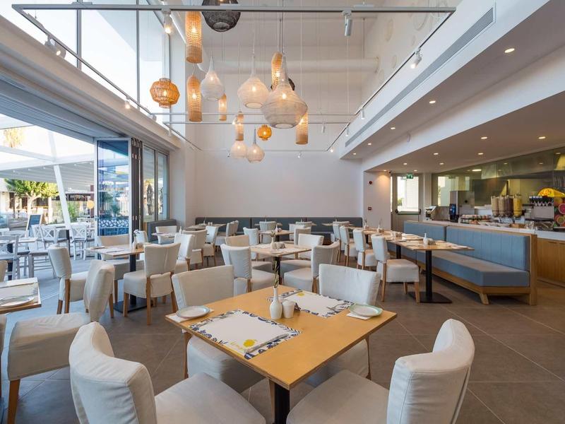 Modernes Restaurant mit hellen Stühlen, Holztischen und großen Fenstern zum Außenbereich.