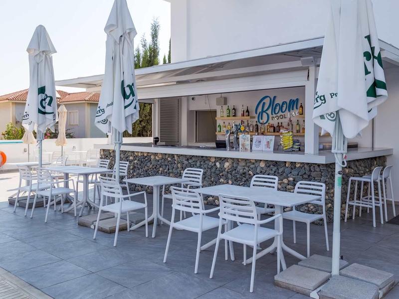 Moderner Außenbereich einer Bar mit weißen Tischen, Stühlen und geschlossenen Sonnenschirmen.