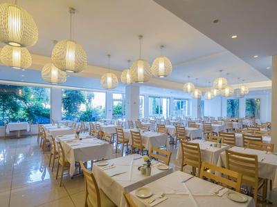 Jasna, nowoczesna restauracja z nakrytymi stołami i dużymi oknami z widokiem na palmy.