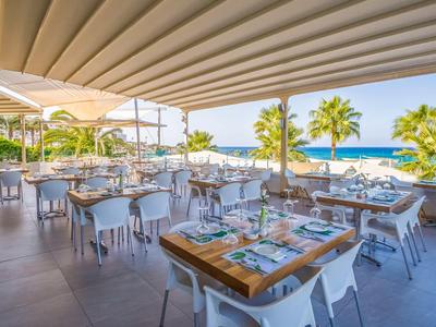 Restauracja na świeżym powietrzu z widokiem na morze, nakrytymi stolikami i palmami w tle.