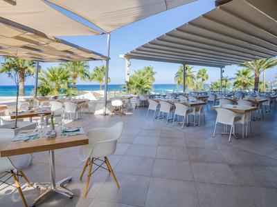 Otwarta taras hotelowy z stolikami, krzesłami, parasolami i widokiem na morze.