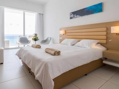 Nowoczesny pokój hotelowy z łóżkiem podwójnym, szafkami nocnymi i widokiem na morze przez duże okna.