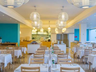 Nowoczesna, jasna jadalnia z drewnianymi stołami i krzesłami, ozdobnymi lampami i dużymi oknami.