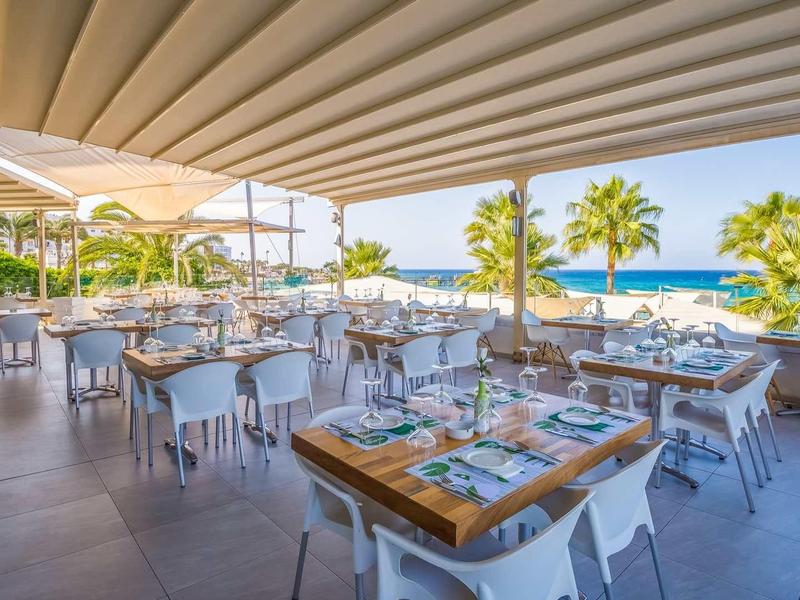 Otwarta restauracja z widokiem na morze, nowoczesne stoły, krzesła i palmy na tarasie.