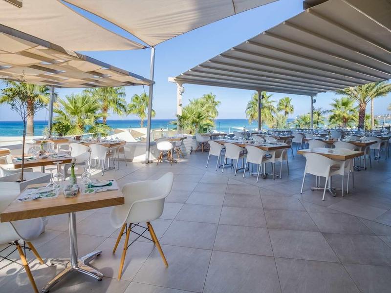 Otwarta taras hotelowy z stolikami, krzesłami, parasolami i widokiem na morze.