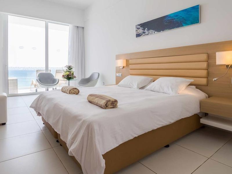 Nowoczesny pokój hotelowy z łóżkiem podwójnym, szafkami nocnymi i widokiem na morze przez duże okna.