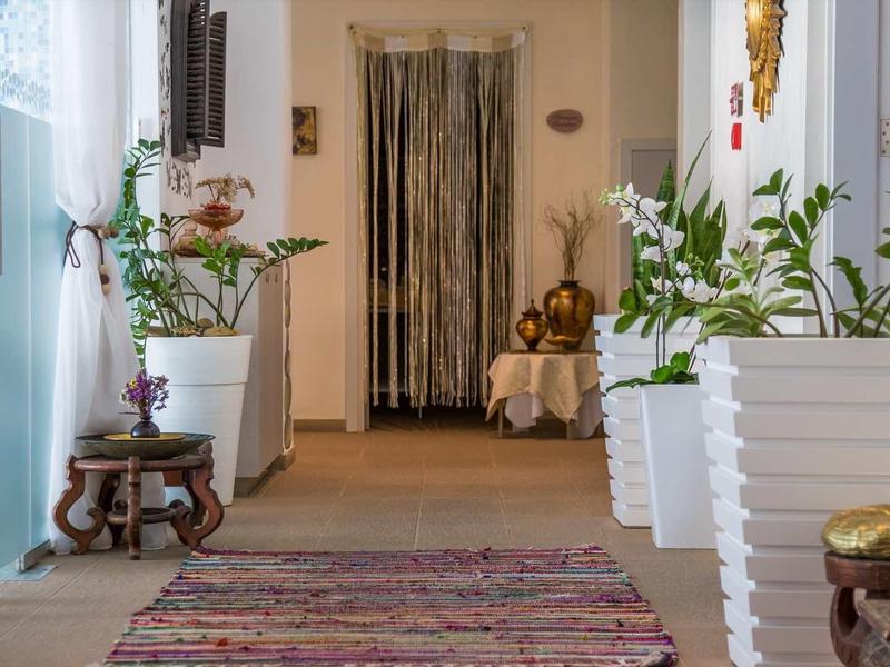 Korytarz z orientalnym dywanem, białymi doniczkami i roślinami, przytulna atmosfera hotelowa.