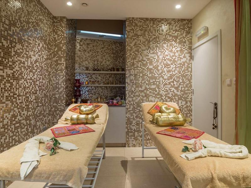 Spokojny pokój spa z dwoma stołami do masażu, ozdobiony ręcznikami i płatkami kwiatów.