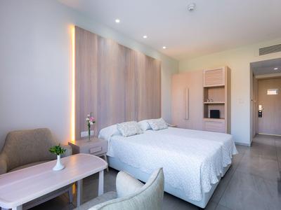 Modern hotel room with double bed, armchairs, table, and soft lighting.