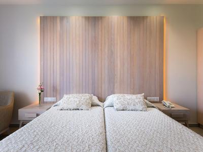 Modern hotel room with two single beds, wooden headboard, and subtle lighting.