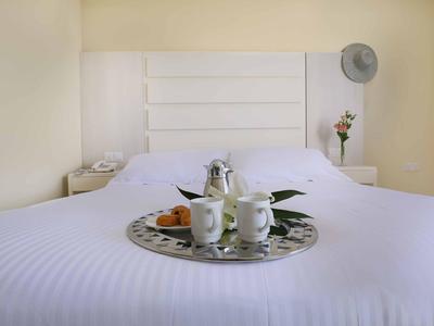 A cozy hotel room with a white bed and a tray with coffee and fruit.